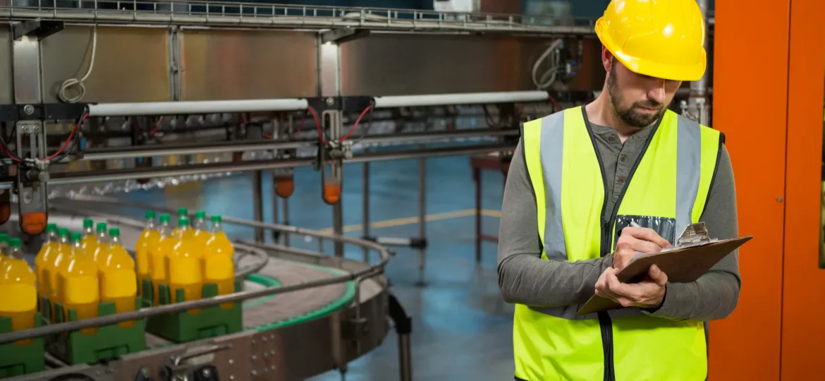 Serious male worker writing on clipboard at juice factory